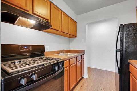 A kitchen with a black refrigerator, wooden cabinets, and a black stove top oven.