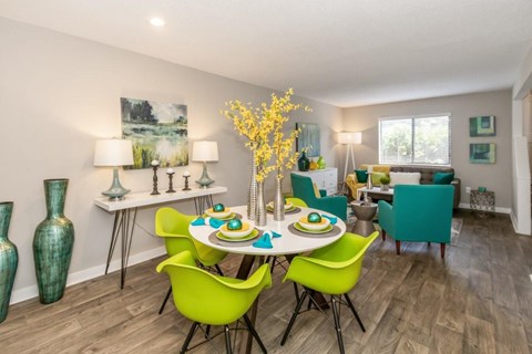 A dining room with a table set for four and green chairs.