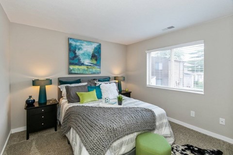 A bedroom with a bed, two lamps, and a painting on the wall.