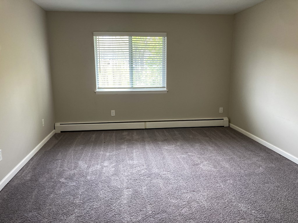 A room with a carpeted floor and a window with blinds.