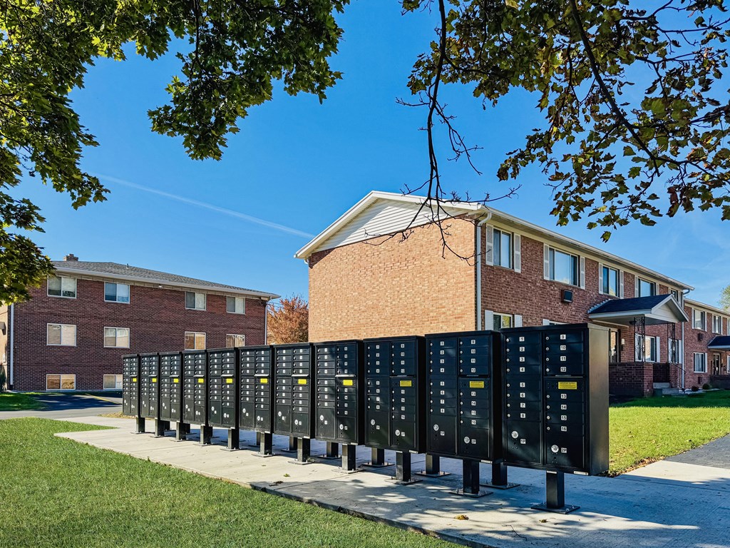 A series of black mailboxes are lined up on a sidewalk in front of a brick building.