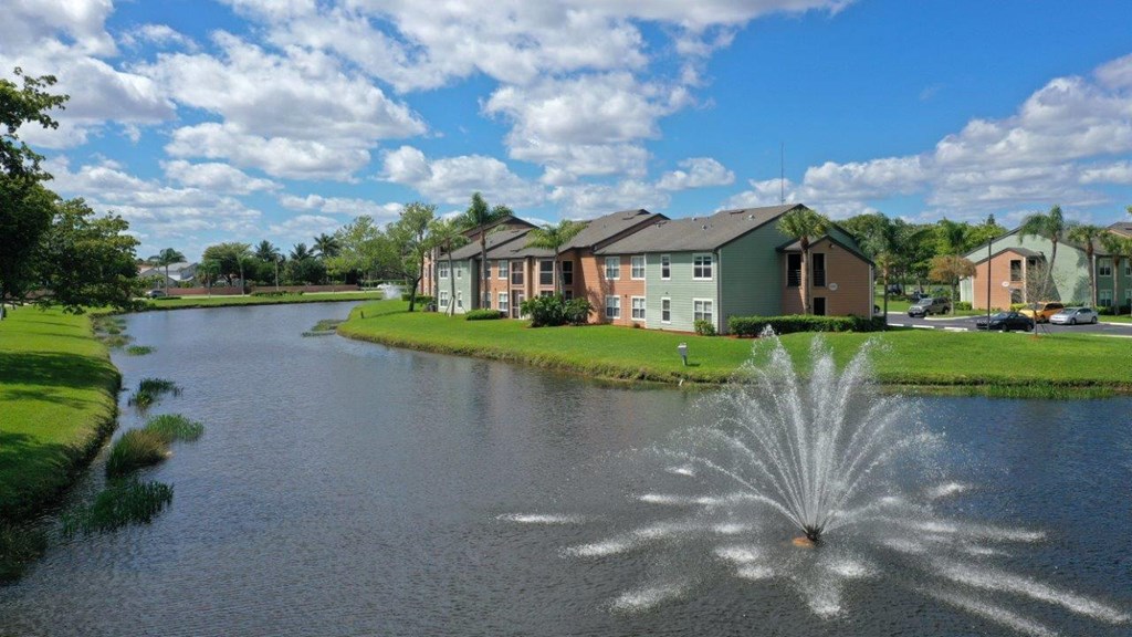 A fountain in the middle of a lake in front of a building.