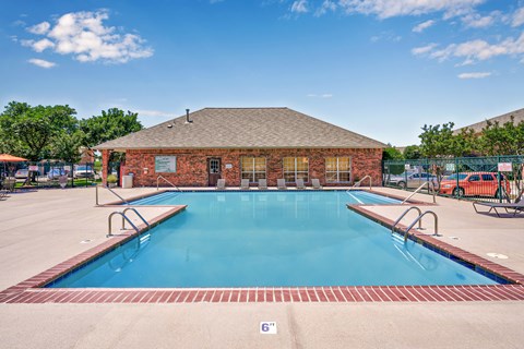 A large outdoor swimming pool with a red brick building in the background.