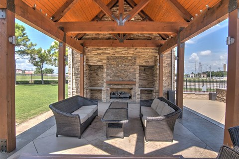 A patio with a stone fireplace and wicker furniture.