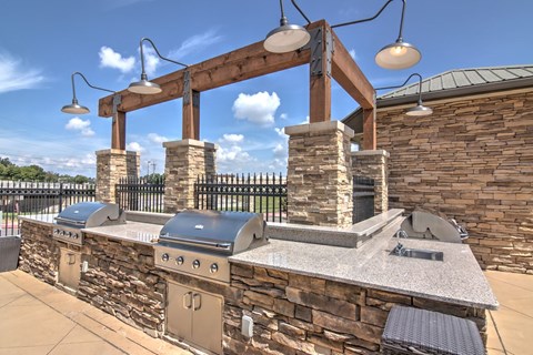 A stone wall with a grill and a pergola.