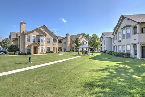 A sunny day at a well-maintained housing complex with a large grassy area in the foreground.