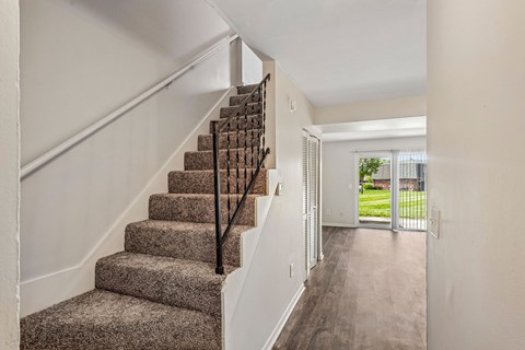 A staircase with a carpeted runner and wooden balusters leads to a bright open space.