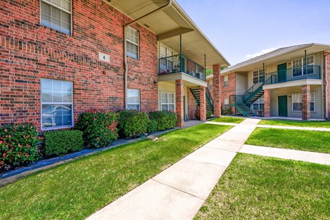 A red brick apartment building with a green lawn in front.
