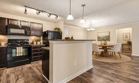A modern kitchen with dark brown cabinets and a wooden floor.