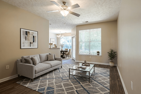 A living room with a grey couch, a glass coffee table, and a ceiling fan.