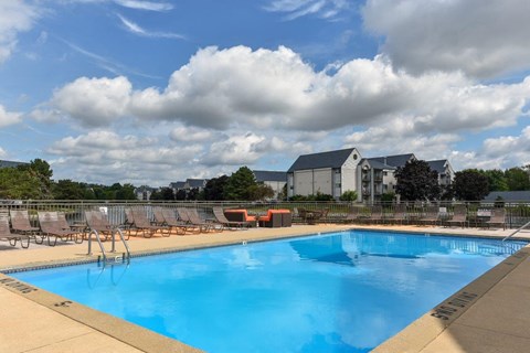 A large swimming pool with a blue tinted water and a cloudy sky in the background.