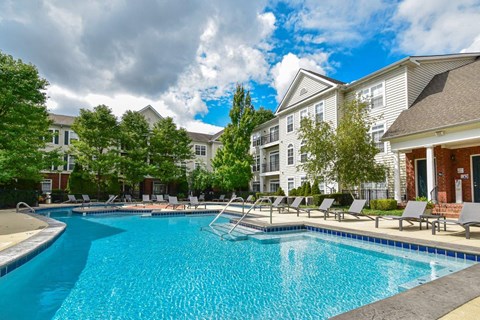 A swimming pool surrounded by lounge chairs and trees in front of apartment buildings.