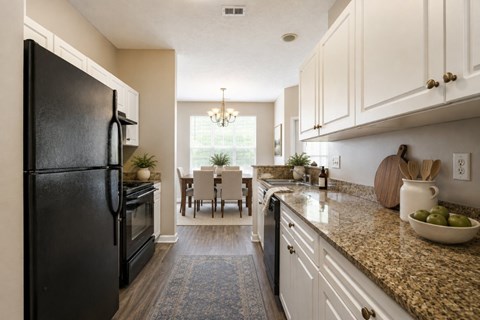 A black refrigerator is on the left in a kitchen with granite countertops and white cabinets.