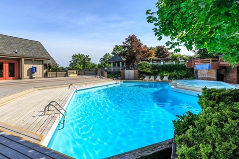 A large outdoor swimming pool surrounded by a wooden deck and greenery.