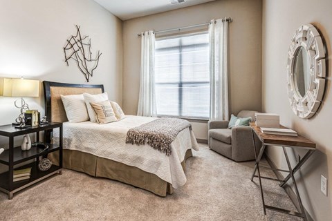 A bedroom with a large bed, a chair, and a mirror on the wall.