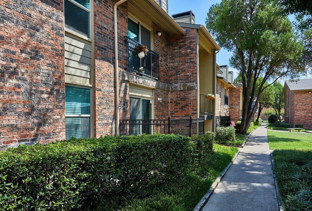 A brick building with a balcony and a hedge in front.