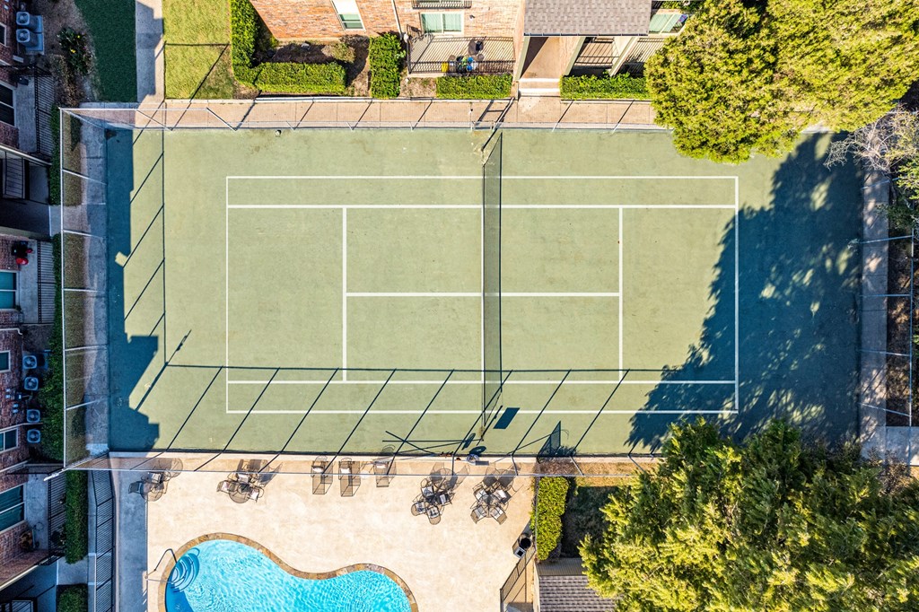 An aerial view of a tennis court surrounded by trees and a pool.