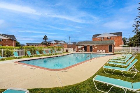 A large outdoor swimming pool surrounded by sun loungers and a building in the background.