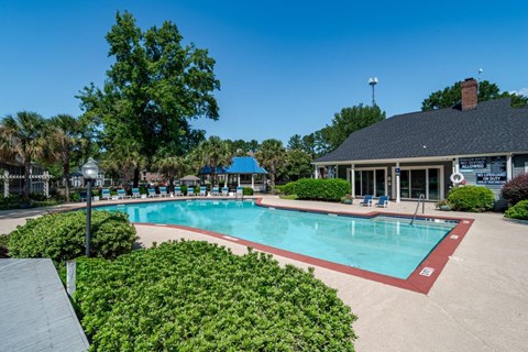 A pool surrounded by green bushes and a building in the background.
