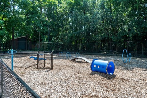 A playground with a blue barrel and a swing set.