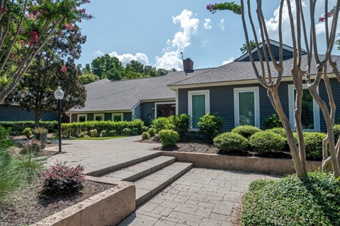 A house with a grey roof and a blue exterior is surrounded by a garden with a brick pathway leading to the front door.