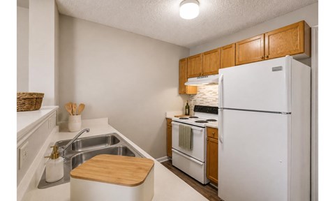 A kitchen with a white refrigerator, a sink, and wooden cabinets.