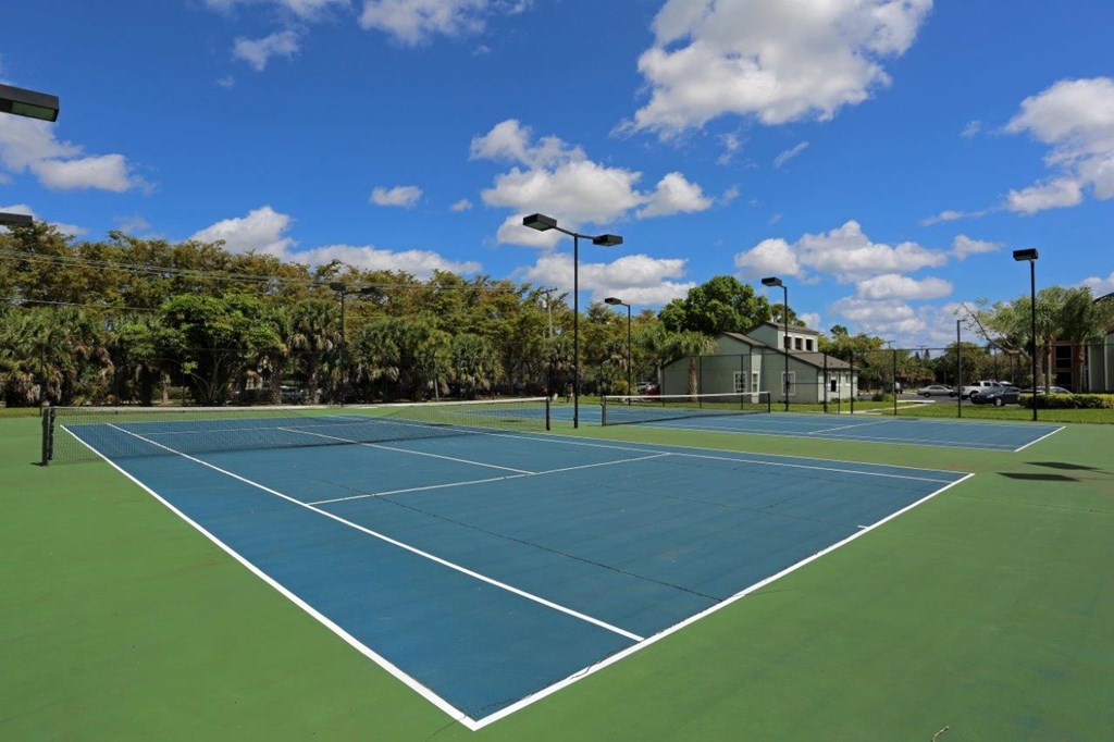 A tennis court surrounded by trees and a cloudy sky.