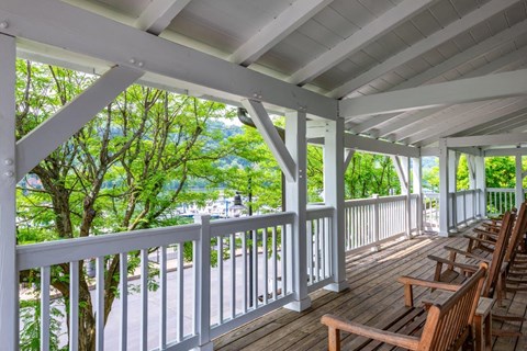 a covered porch with wooden chairs and a view of a body of water