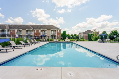 A large swimming pool with lounge chairs and apartment buildings in the background.