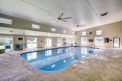 A large indoor swimming pool with a ceiling fan and multiple windows.