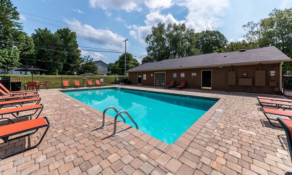 a swimming pool with chairs around it in front of a house