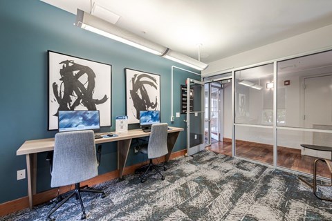 A room with a desk and chairs and two framed pictures on the wall.