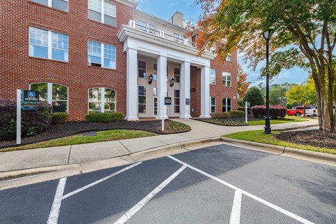 A building with a white entrance and pillars is surrounded by trees and a parking lot.