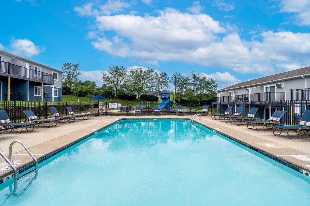 A large swimming pool surrounded by sun loungers and apartment buildings.