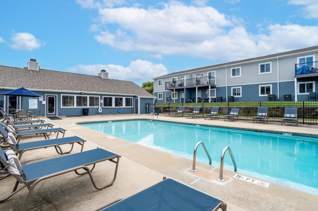 A pool area with chairs and a building in the background.