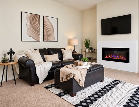 A living room with a black couch, a fireplace, and a TV mounted on the wall.