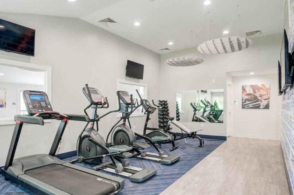 a gym with cardio equipment and a tv on the wall