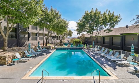 A large swimming pool surrounded by lounge chairs and trees.