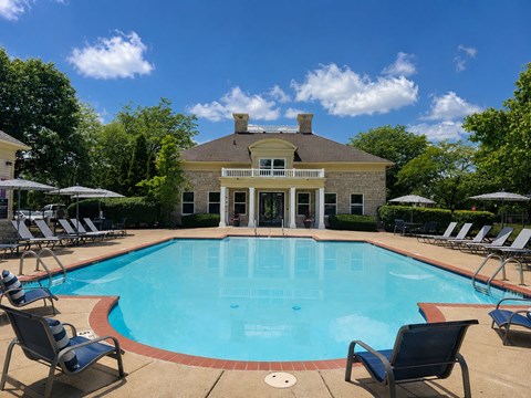 A pool with chairs around it and a house in the background.