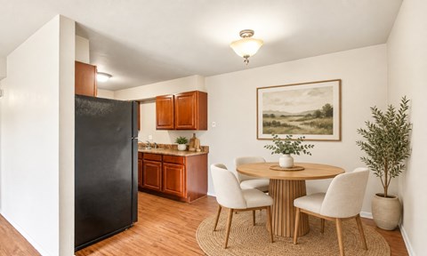 A kitchen with a black refrigerator, wooden cabinets, a round table with chairs, and a painting on the wall.