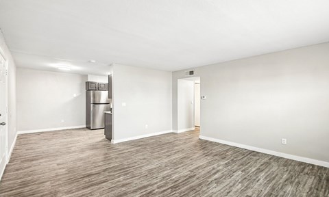 A spacious room with a wooden floor and a refrigerator in the corner.