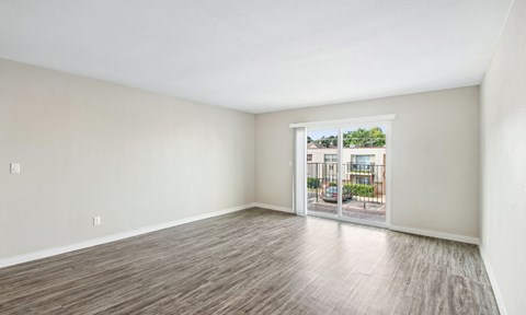 A room with a sliding glass door leading to a balcony with a view of a building and trees.