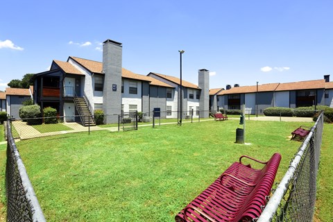 A red bench sits in the middle of a grassy area in front of a building.