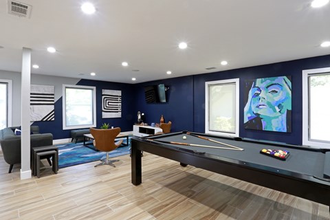 A pool table is in the middle of a room with a blue wall and a painting of a woman's face.