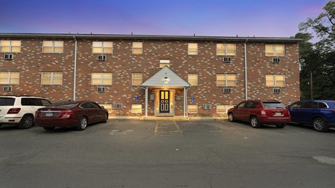 A parking lot in front of a brick building with cars parked.