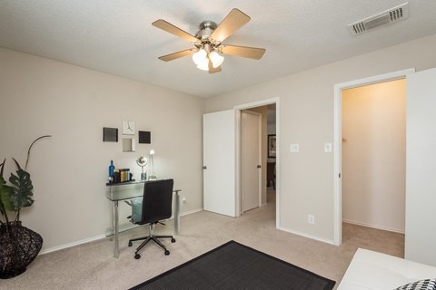 A room with a ceiling fan and a desk with a chair.