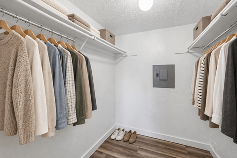 A row of sweaters hang on a rack in a white room.