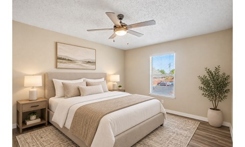 A bedroom with a bed, two lamps, a ceiling fan, and a plant.