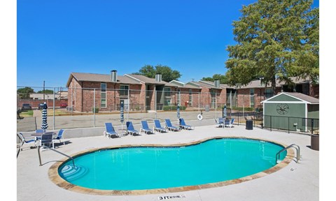 A pool surrounded by chairs and a building in the background.