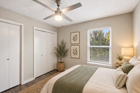 A bedroom with a bed, a ceiling fan, and a window with blinds.